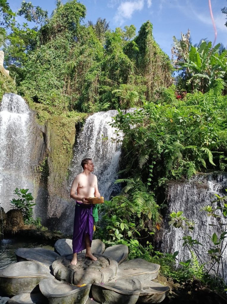 Un expatrié en sarong violet participe au rituel de purification Melukat devant les cascades du Beji Griya Park à Bali.