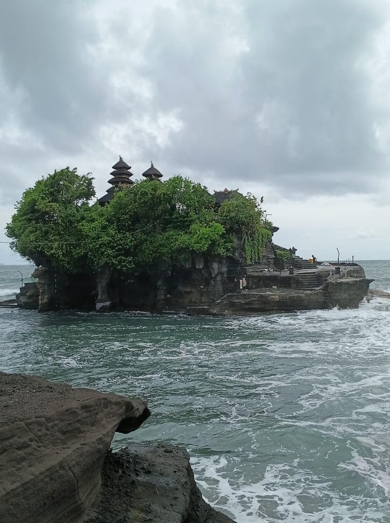 Vue du temple hindou de Pura Tanah Lot perché sur son rocher entouré par l'océan Indien sous un ciel nuageux à Bali.