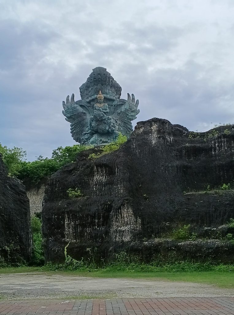 La statue géante en cuivre et laiton de l'oiseau mythique Garuda s'élevant derrière des falaises de calcaire noir au parc culturel GWK à Bali.