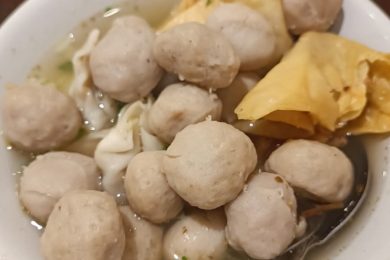 Un bol de soupe Bakso rempli de boulettes de viande rondes et de morceaux de wonton frits croustillants, avec une cuillère posée à l'intérieur.