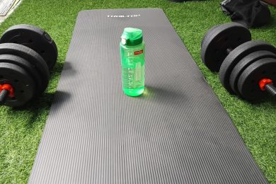 Tapis de yoga noir, haltères et gourde verte posés sur du gazon artificiel pour une séance de fitness à Bali.