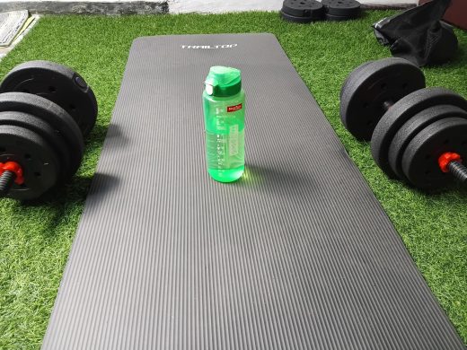 Tapis de yoga noir, haltères et gourde verte posés sur du gazon artificiel pour une séance de fitness à Bali.