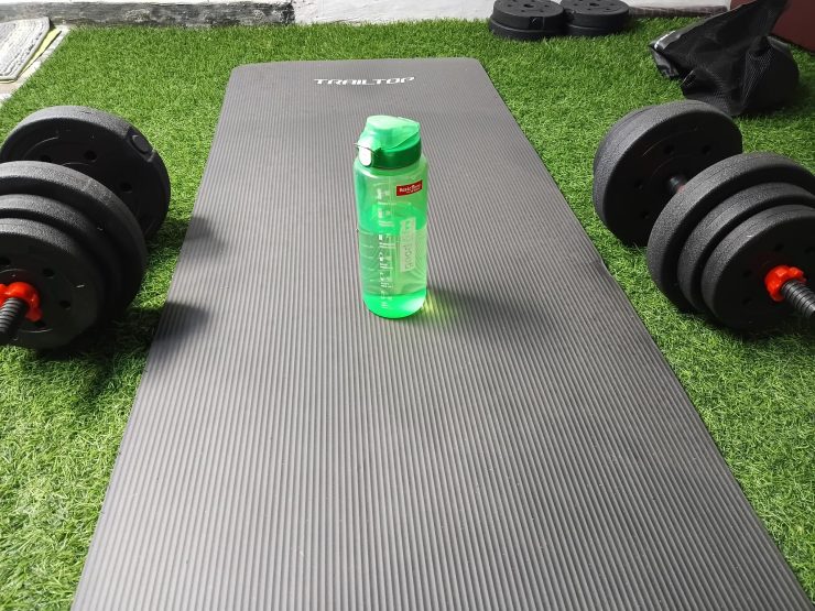 Tapis de yoga noir, haltères et gourde verte posés sur du gazon artificiel pour une séance de fitness à Bali.